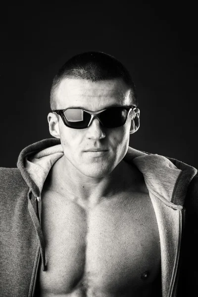 Uomo muscoloso in giacca sportiva e occhiali scuri su sfondo nero . — Foto Stock