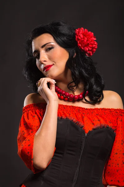 Karanlık bir arka plan üzerinde kırmızı ve siyah elbiseli güzel bir genç kadın portresi.