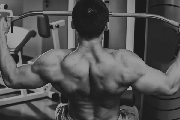 Homem musculoso forte fazendo exercícios no ginásio. Corpo bonito em uma foto em preto e branco. Estilo de vida saudável . — Fotografia de Stock