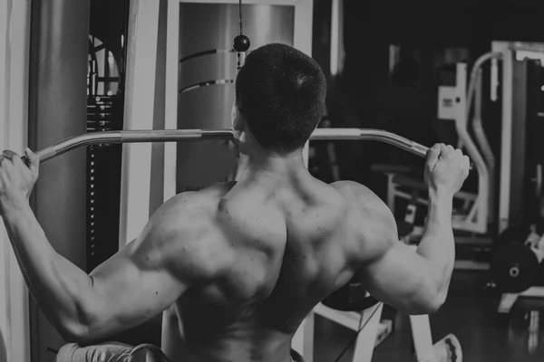 Strong muscular man doing exercises in the gym. Beautiful body on a black and white photo. Healthy lifestyle. — Stock Photo, Image