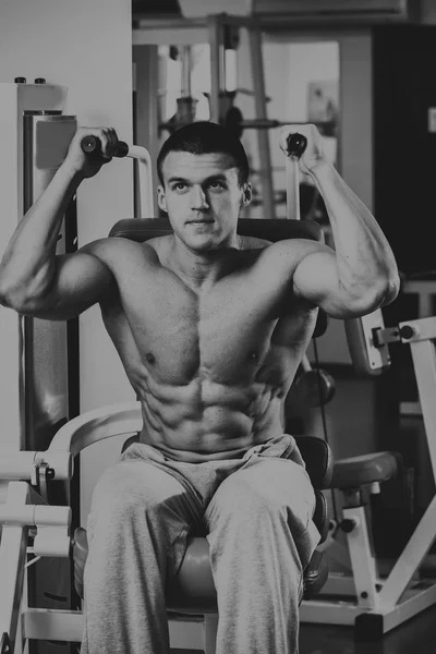 Forte uomo muscolare che fa esercizi in palestra. Bellissimo corpo su una foto in bianco e nero. Stile di vita sano . — Foto Stock