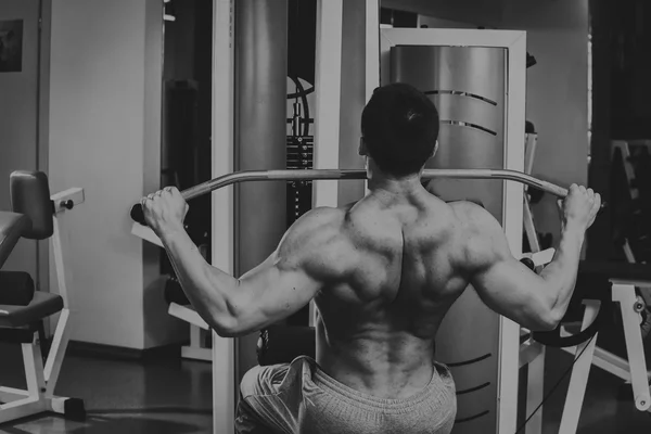 Un bărbat puternic musculos face exerciții în sala de gimnastică. Corp frumos pe o fotografie alb-negru. Un stil de viață sănătos . — Fotografie, imagine de stoc