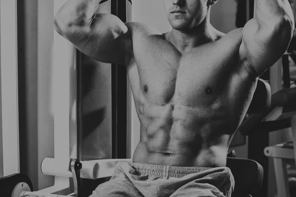 Sterke gespierde man doen oefeningen in de sportschool. Mooi lichaam op een zwart-wit foto. Gezonde levensstijl. — Stockfoto