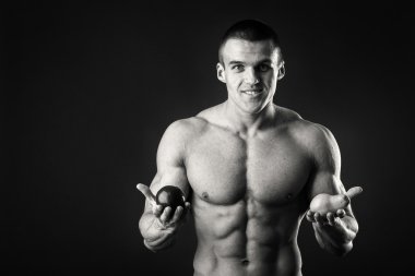 Vücut geliştirmeci bir meyve karanlık bir arka plan üzerinde tutarak. Gösteri profesyonel atlet sağlıklı beslenme.