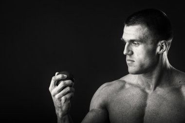 Vücut geliştirmeci bir meyve karanlık bir arka plan üzerinde tutarak. Gösteri profesyonel atlet sağlıklı beslenme.