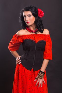 Karanlık bir arka plan üzerinde kırmızı ve siyah elbiseli güzel bir genç kadın portresi.