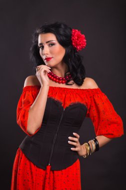 Karanlık bir arka plan üzerinde kırmızı ve siyah elbiseli güzel bir genç kadın portresi.