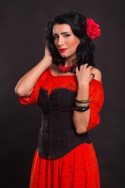 Karanlık bir arka plan üzerinde kırmızı ve siyah elbiseli güzel bir genç kadın portresi.