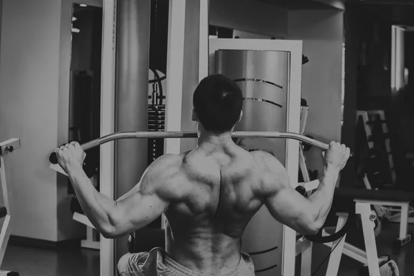 Starker muskulöser Mann bei Übungen im Fitnessstudio. schöner Körper auf einem Schwarz-Weiß-Foto. Gesunder Lebensstil. — Stockfoto