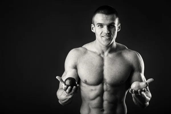Bodybuilder innehar en frukt på en mörk bakgrund. Demonstration professionell idrottsman hälsosam kost. — Stockfoto