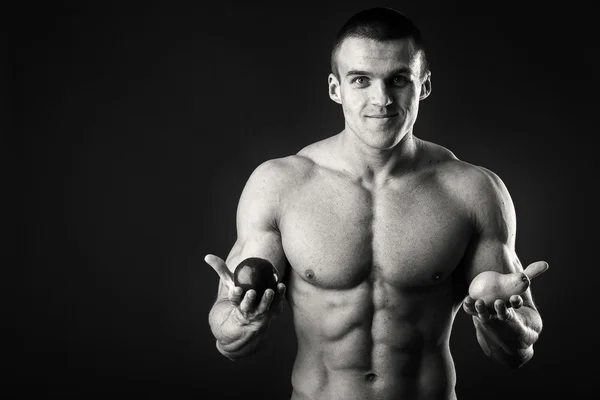 Bodybuilder mit einer Frucht auf dunklem Hintergrund. Demonstration professioneller Sportler gesunde Ernährung. — Stockfoto
