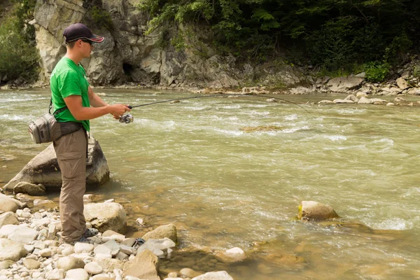 Pescatore sportivo mostra trota di cattura in un fiume di montagna. Interessante e pericoloso confronto tra pescatori e pesci. Riposo sano ed emotivo su un fiume di montagna. Foto riviste di pesca — Foto Stock