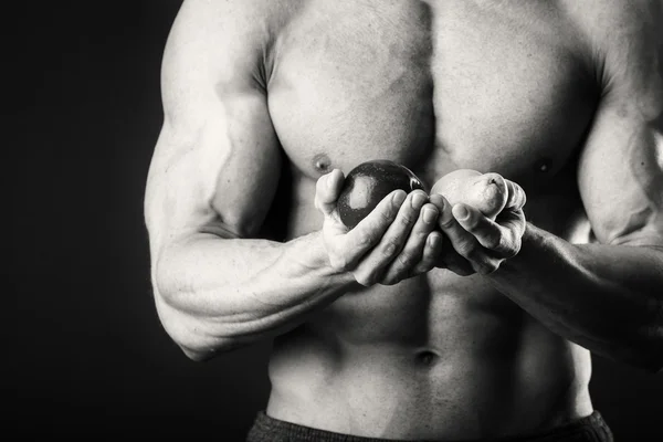 Bodybuilder houden een vrucht op een donkere achtergrond. Demonstratie professionele atleet gezonde voeding. — Stockfoto