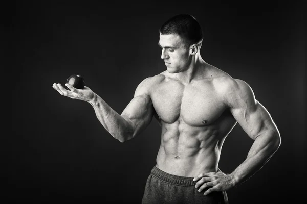 Culturista sosteniendo una fruta sobre un fondo oscuro. Demostración atleta profesional dieta saludable . —  Fotos de Stock