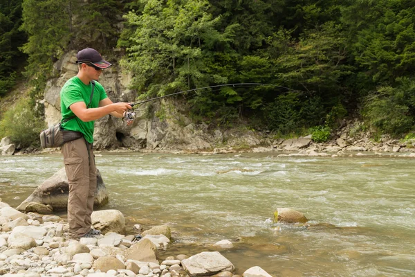 Pescatore sportivo mostra trota di cattura in un fiume di montagna. Interessante e pericoloso confronto tra pescatori e pesci. Riposo sano ed emotivo su un fiume di montagna. Foto riviste di pesca — Foto Stock