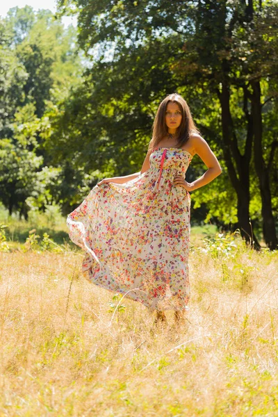 Uma menina jovem e atraente em belo vestido de verão no meio de prados ensolarados. Menina alegre se aquecendo nos raios quentes do sol de verão. Imagem bonita de uma menina despreocupada. Fotos para revistas , — Fotografia de Stock