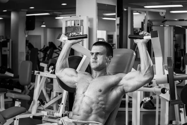 Ισχυρή μυώδης άνδρας κάνει ασκήσεις στο γυμναστήριο. Όμορφο σώμα σε μια ασπρόμαυρη φωτογραφία. Υγιεινός τρόπος ζωής. — Φωτογραφία Αρχείου
