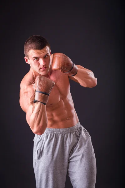 Muscular man in boxing gloves on a dark background. Professional boxer boxing shows muscle in racks. Beautiful muscular body boxer. Photos for sporting magazines, posters and websites. — Stock Photo, Image