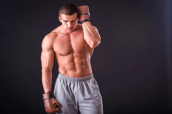 Homem musculoso com luvas de boxe num fundo escuro. Boxe boxeador profissional mostra músculo em racks. Bonito boxeador muscular. Fotos para revistas esportivas, cartazes e sites . — Fotografia de Stock