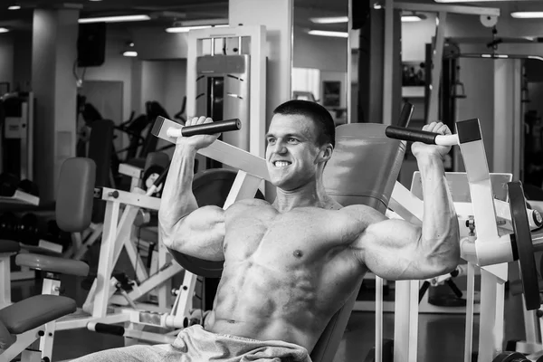 Silne muskularny mężczyzna robi ćwiczenia na siłowni. Piękne ciało na czarno-białe zdjęcie. Zdrowy styl życia. — Zdjęcie stockowe