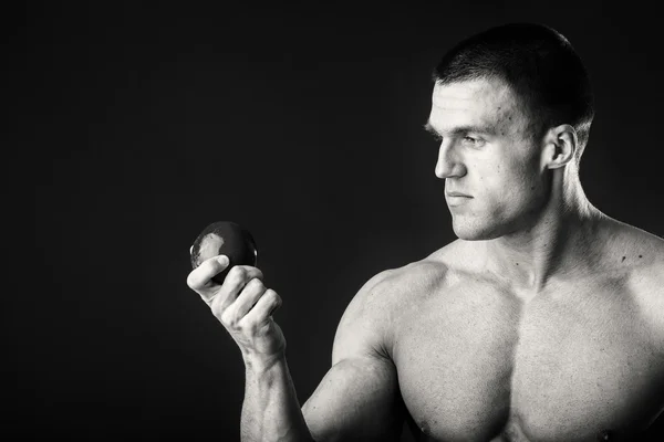 Kulturysta trzymając owoce na ciemnym tle. Pokaz profesjonalnego sportowca zdrowej diety. — Zdjęcie stockowe