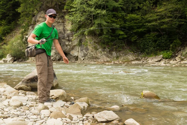 Sportsman fisherman shows catch trout in a mountain river. Interesting and hazardous confrontation between fishermen and fish. Healthy and emotional rest on a mountain river. Photo fishing magazines