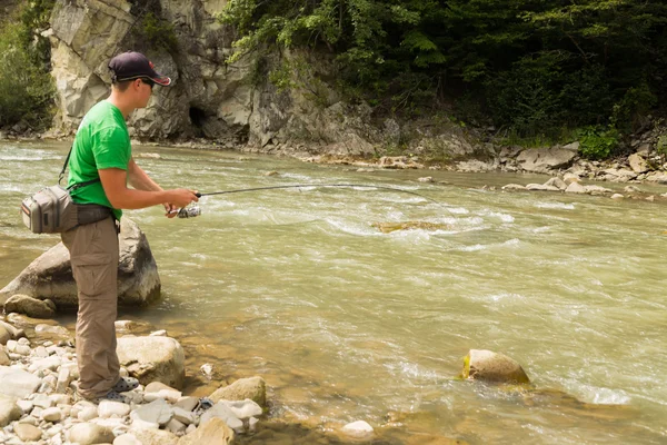 Pescatore sportivo mostra trota di cattura in un fiume di montagna. Interessante e pericoloso confronto tra pescatori e pesci. Riposo sano ed emotivo su un fiume di montagna. Foto riviste di pesca — Foto Stock