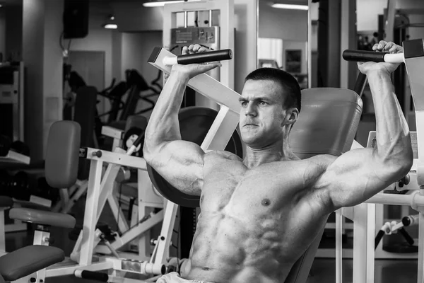 Strong muscular man doing exercises in the gym. Beautiful body on a black and white photo. Healthy lifestyle. — Stock Photo, Image