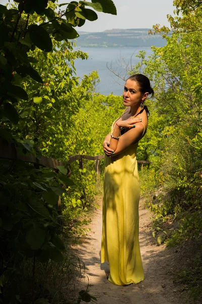 Retrato da menina contra o pano de fundo de uma bela paisagem natural. Menina na natureza em um belo vestido amarelo . — Fotografia de Stock
