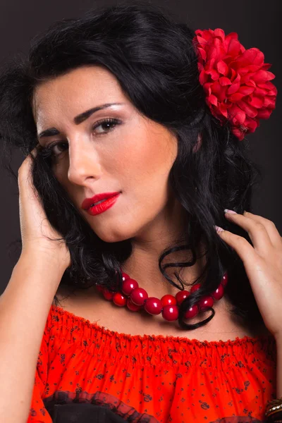 Karanlık bir arka plan üzerinde kırmızı ve siyah elbiseli güzel bir genç kadın portresi.