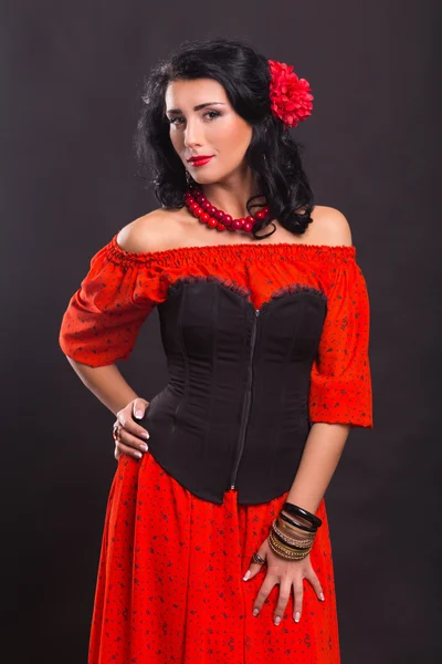 Karanlık bir arka plan üzerinde kırmızı ve siyah elbiseli güzel bir genç kadın portresi.