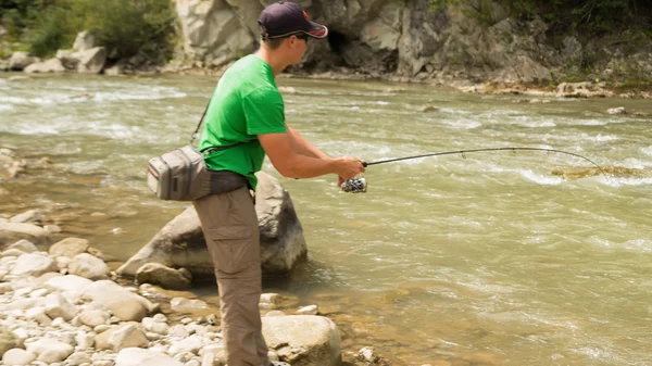 Pescatore sportivo mostra trota di cattura in un fiume di montagna. Interessante e pericoloso confronto tra pescatori e pesci. Riposo sano ed emotivo su un fiume di montagna. Foto riviste di pesca — Foto Stock