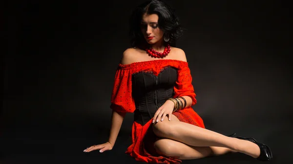 Portret van een mooie jonge vrouw in rode en zwarte jurk op een donkere achtergrond. — Stockfoto