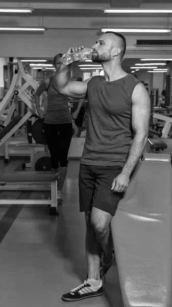 Een sterke man in de sportschool. Rust tussen de oefeningen. Knappe man drinkt water. — Stockfoto