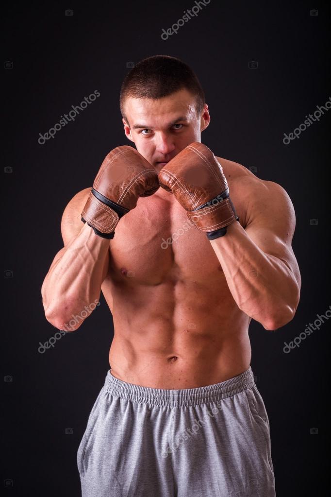 Muscular man in boxing gloves on a dark background. Professional boxer