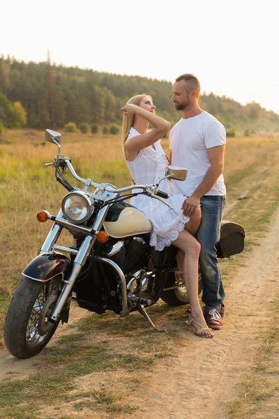 Biker und schöne Mädchen in einem Feld auf einem Motorrad. — Stockfoto