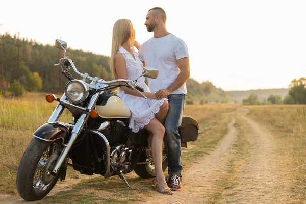 Biker and beautiful girl in a field on a motorcycle. — Stock Photo, Image