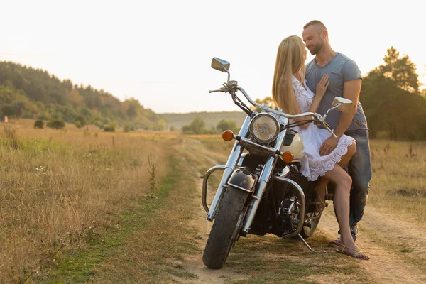 Biker and beautiful girl in a field on a motorcycle. — Stock Photo, Image
