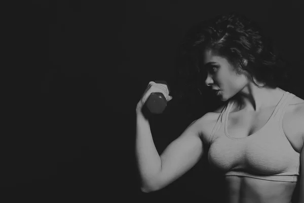 Zwart-wit foto van mooie atleet op een donkere achtergrond. Fitness voor vrouwen. Werken met halters. Foto's voor sportieve tijdschriften, posters en websites. — Stockfoto