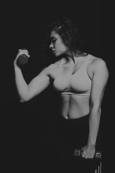 Zwart-wit foto van mooie atleet op een donkere achtergrond. Fitness voor vrouwen. Werken met halters. Foto's voor sportieve tijdschriften, posters en websites. — Stockfoto