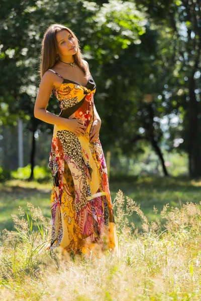 A young and attractive girl in beautiful summer dress middle of sunny meadows. Cheerful girl basking in the warm rays of the summer sun. Beautiful image of a carefree girl. Photos for magazines, — Stock Photo, Image