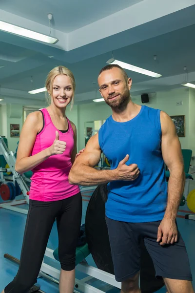 Pareja joven en una sesión de entrenamiento conjunto en el gimnasio. Asistencia mutua en la realización de ejercicios. Ejercicio adecuado. Fotos para revistas deportivas y sociales, carteles y sitios web . —  Fotos de Stock