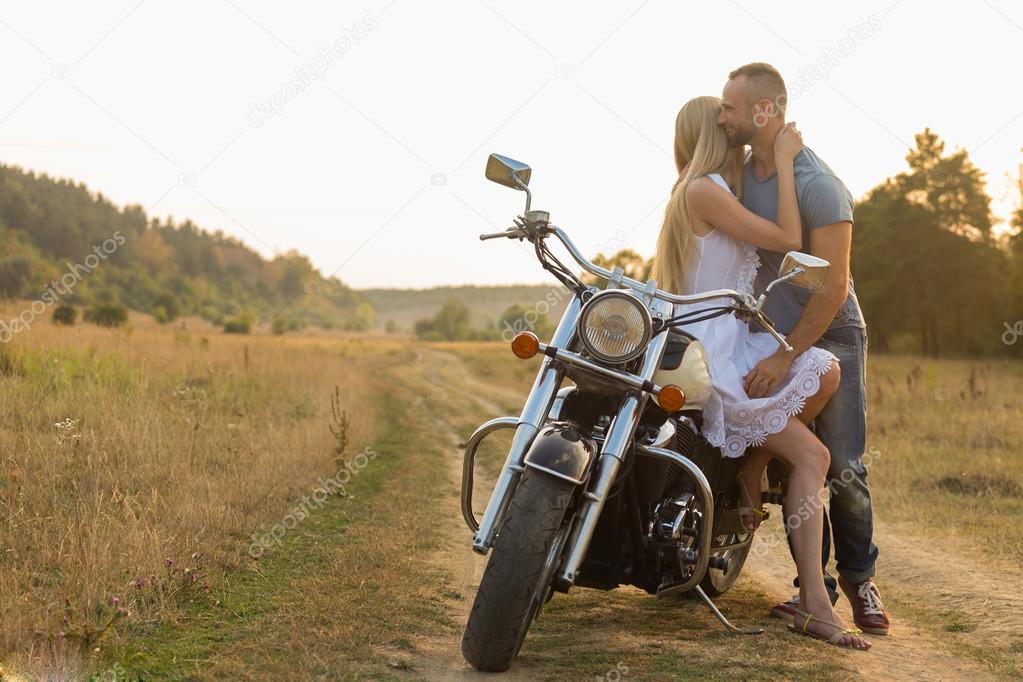 Biker and beautiful girl in a field on a motorcycle.