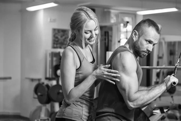 Jong koppel bij een gezamenlijke training in de sportschool. Wederzijdse bijstand bij de uitvoering van de oefeningen. Een goede oefening. Foto's voor sportieve en sociale tijdschriften, posters en websites. — Stockfoto