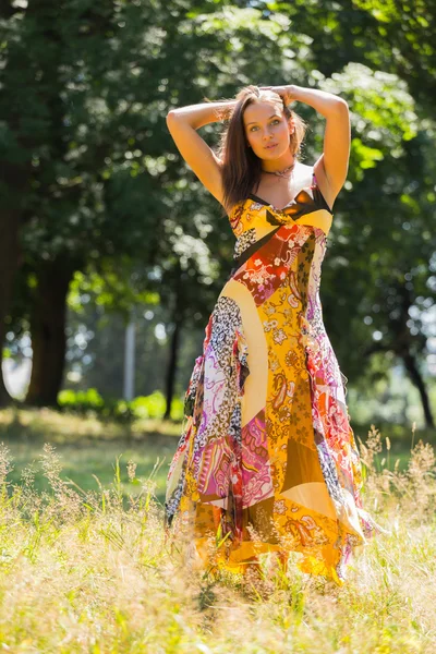 En ung och attraktiv flicka i vacker sommar klänning mitten av soliga ängar. Glad tjej Solar sig i varma strålar från sommarsolen. Vacker bild av en sorglös flicka. — Stockfoto