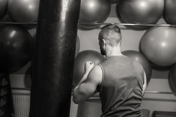 Gespierde man in de sportschool. De man raakte een bokszak, uitoefenen. Boksen, training, spiermassa, kracht, macht - het concept van krachttraining en boksen — Stockfoto