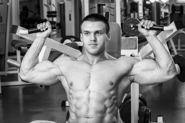 Gespierde man in de sportschool. Werken op de armspieren. Training op een simulator. Vermoeiend werk op zijn lichaam. — Stockfoto