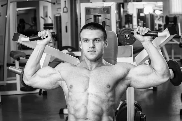 Hombre musculoso en el gimnasio. Trabaja en los músculos del brazo. Entrenamiento en un simulador. Trabajo agotador en su cuerpo . — Foto de Stock