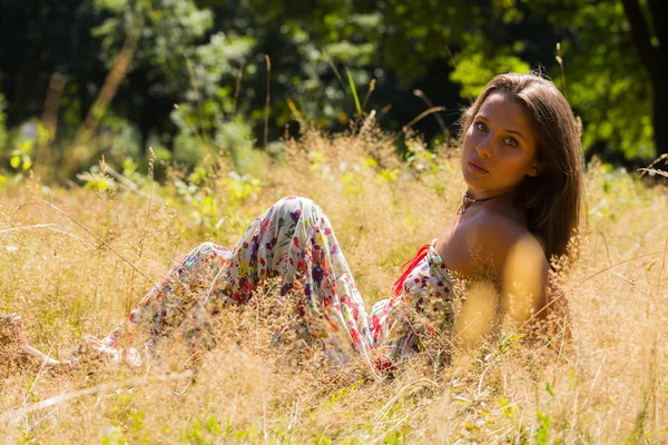 En ung och attraktiv flicka i vacker sommar klänning mitten av soliga ängar. Glad tjej Solar sig i varma strålar från sommarsolen. Vacker bild av en sorglös flicka. — Stockfoto