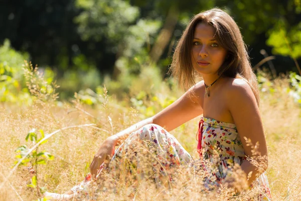 Una chica joven y atractiva en hermoso vestido de verano en medio de prados soleados. Chica alegre tomando el sol en los cálidos rayos del sol de verano. Hermosa imagen de una chica despreocupada . —  Fotos de Stock